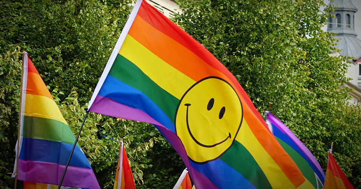 Das Foto zeigt Regenbogenfahnen von Menschen, die an einer Pride-Parade teilnehmen. ©Envato