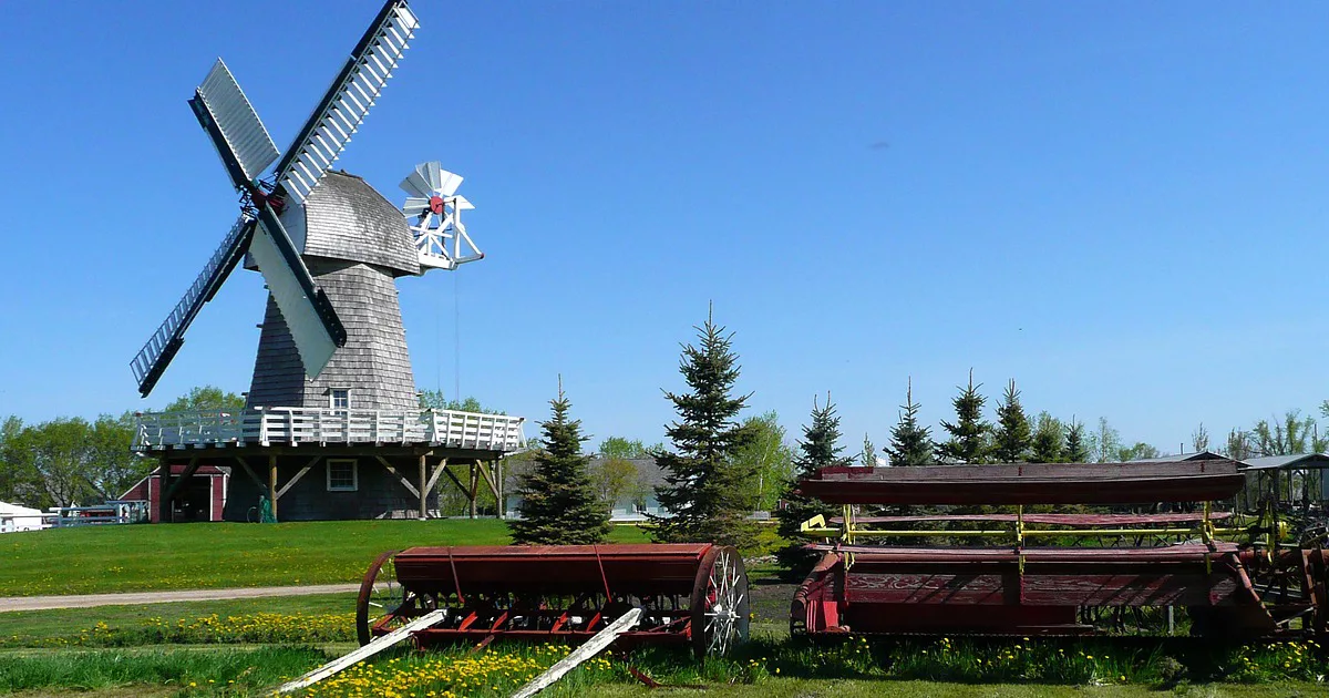 Foto vom Mennonite Heritage Village in Steinbach, Kanada. Abgebildet ist eine Windmühle und landwirtschaftliche Geräte. ©ArtTower by Pixabay